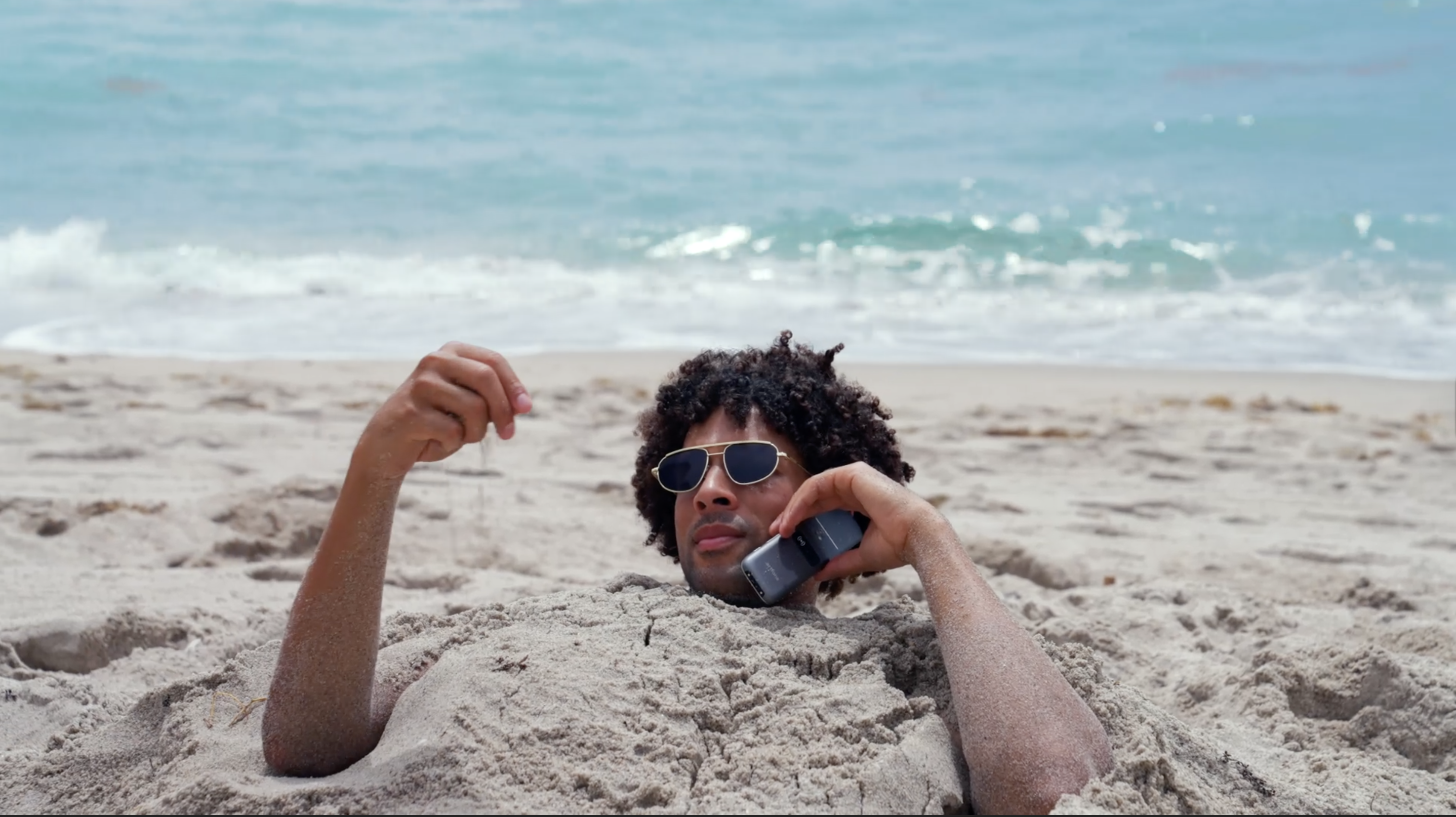 Man buried in the sand at the beach and talking on the phone